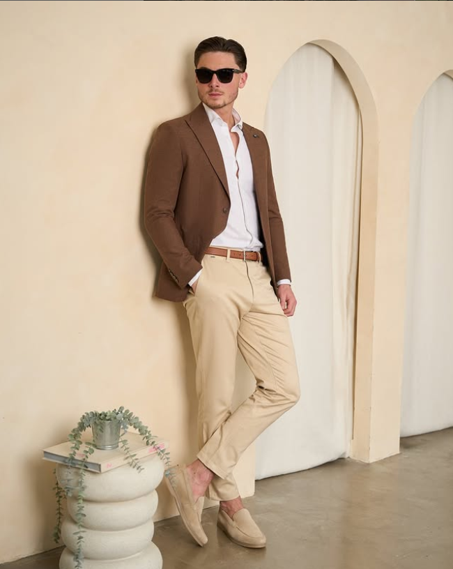 A man wearing suit seprataes standing effortlessly against a wall.