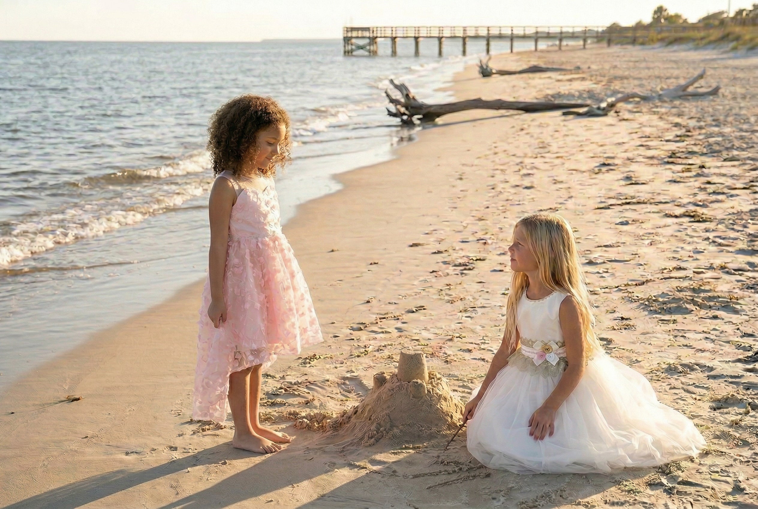 A flower girl in an ivory dress and a junior bridesmaid in a blush pink dress on the beach.