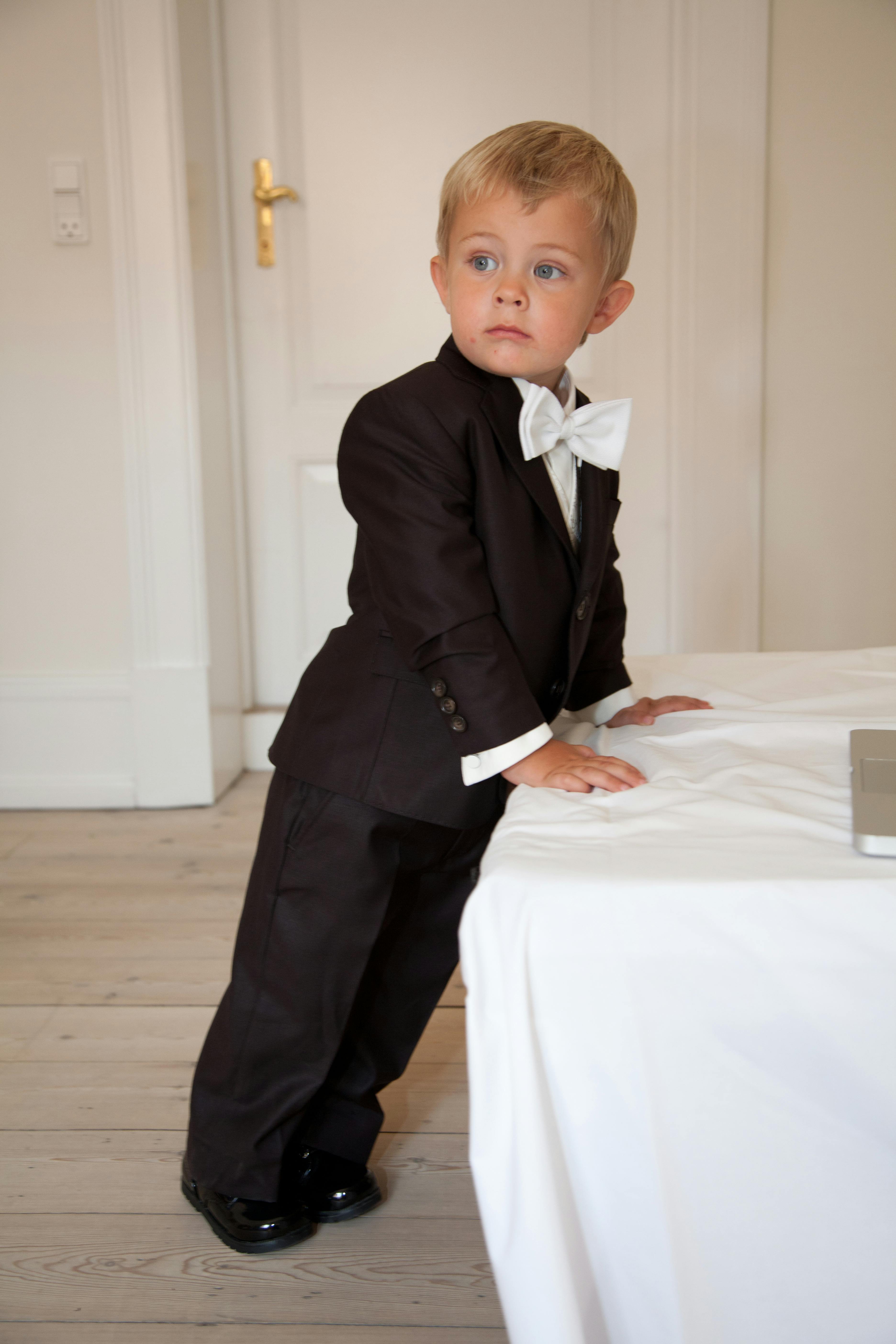 Boy wearing a black suit while leaning on a white cloth.