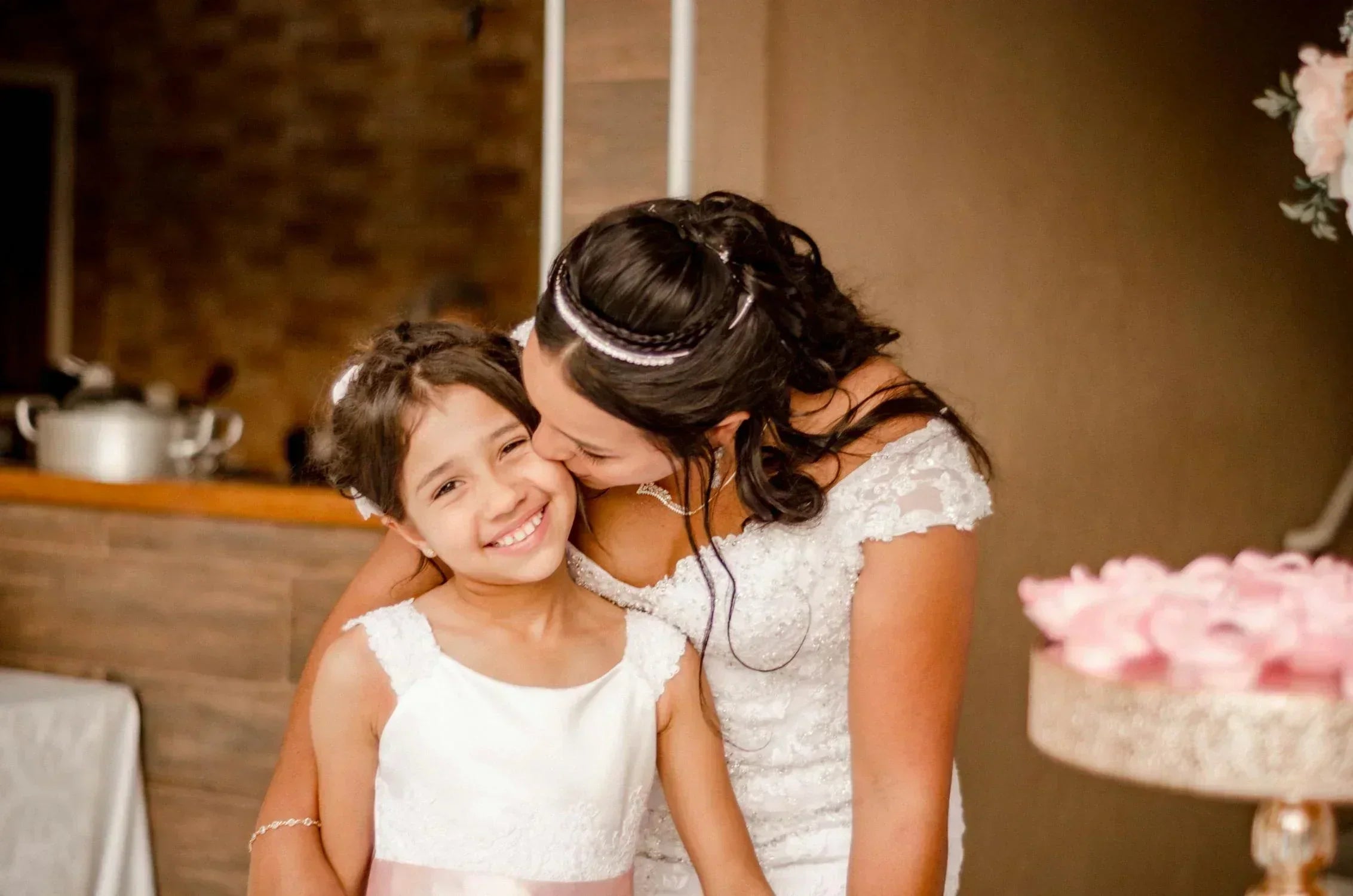 a mother in a wedding dress kissing her junior bridesmaid daughter