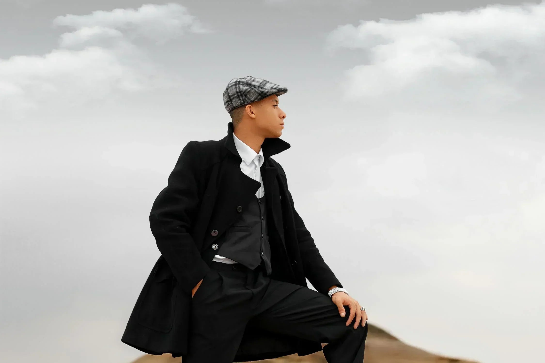 A man in a black coat and hat sitting on a hill